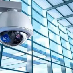 Kamera monitoringu kopułkowa zamontowana na ścianie wewnątrz nowoczesnego budynku z przeszklonymi ścianami i sufitem.