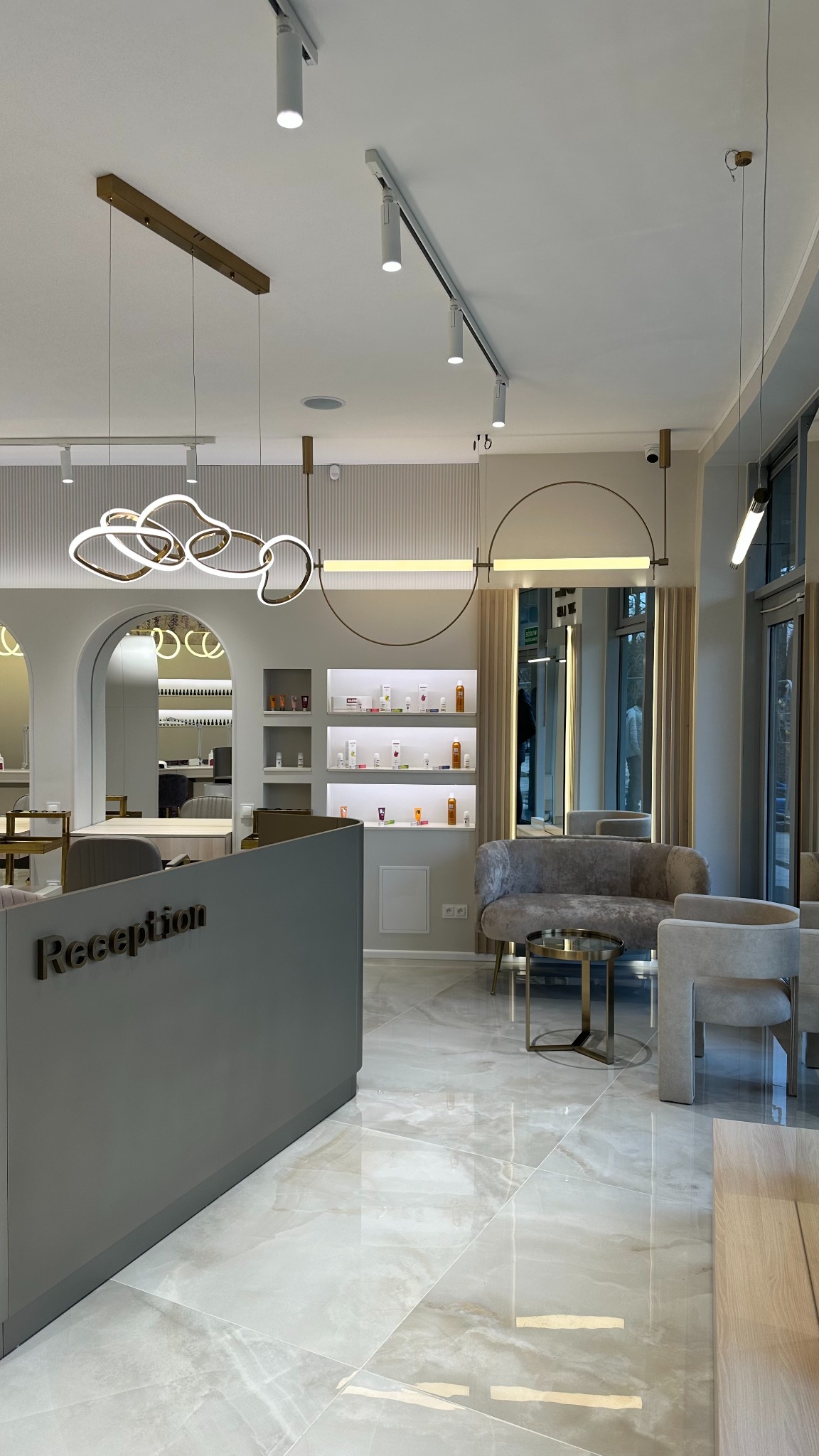 Nowoczesne oświetlenie w eleganckim salonie: lampy wiszące o abstrakcyjnych kształtach, reflektory szynowe i podświetlane półki z produktami, tworzące luksusową atmosferę.