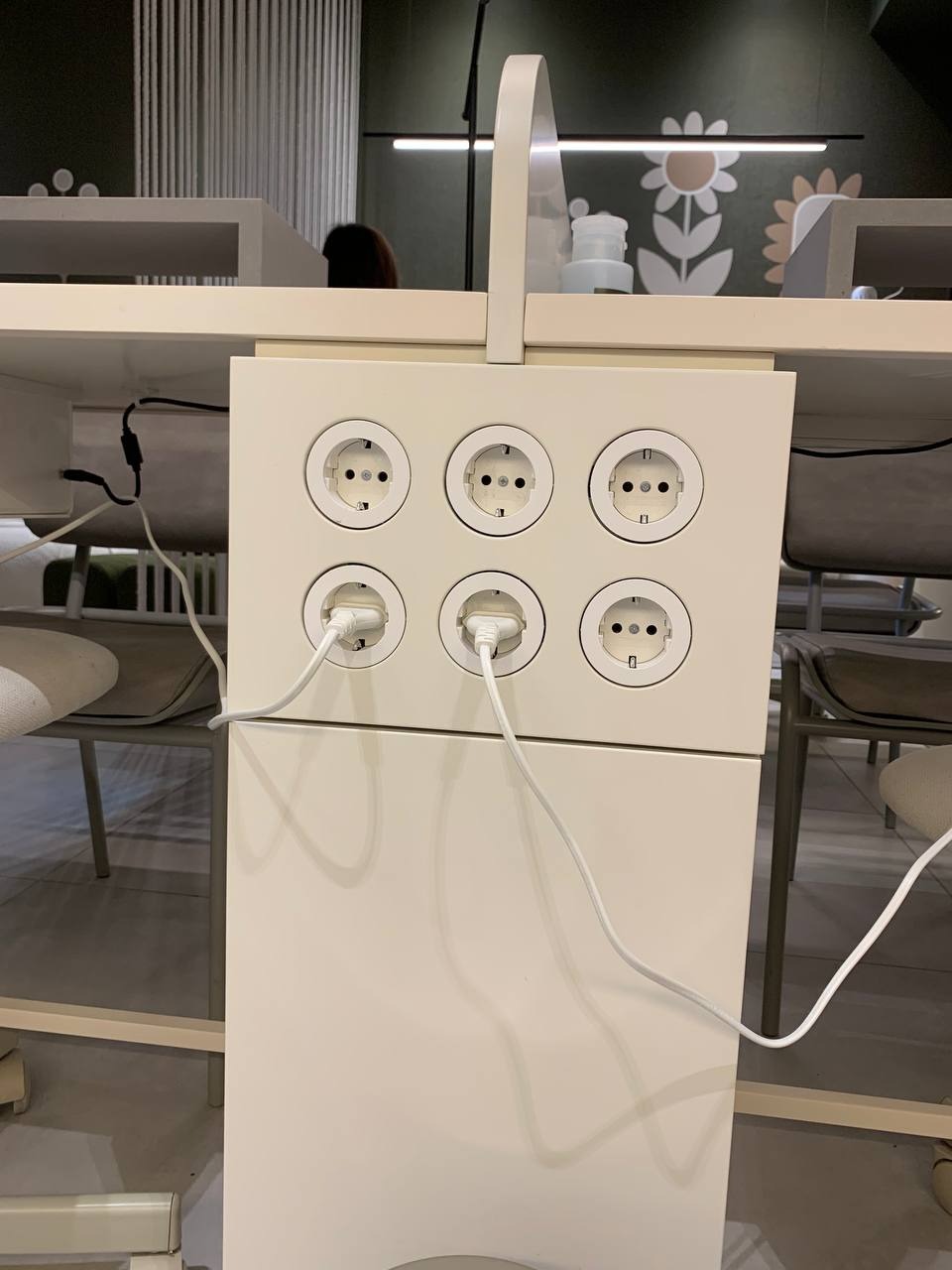 Biała, modułowa listwa zasilająca z sześcioma gniazdami Schuko, z dwoma wpiętymi wtyczkami, umieszczona pod blatem biurka w nowoczesnym biurze.