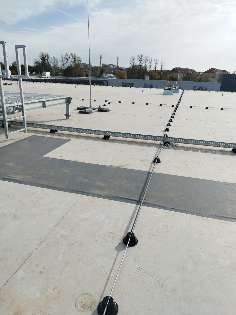 System odgromowy z przewodami na dachu budynku, widoczne uchwyty i maszt odgromowy, w tle zabudowa miejska.