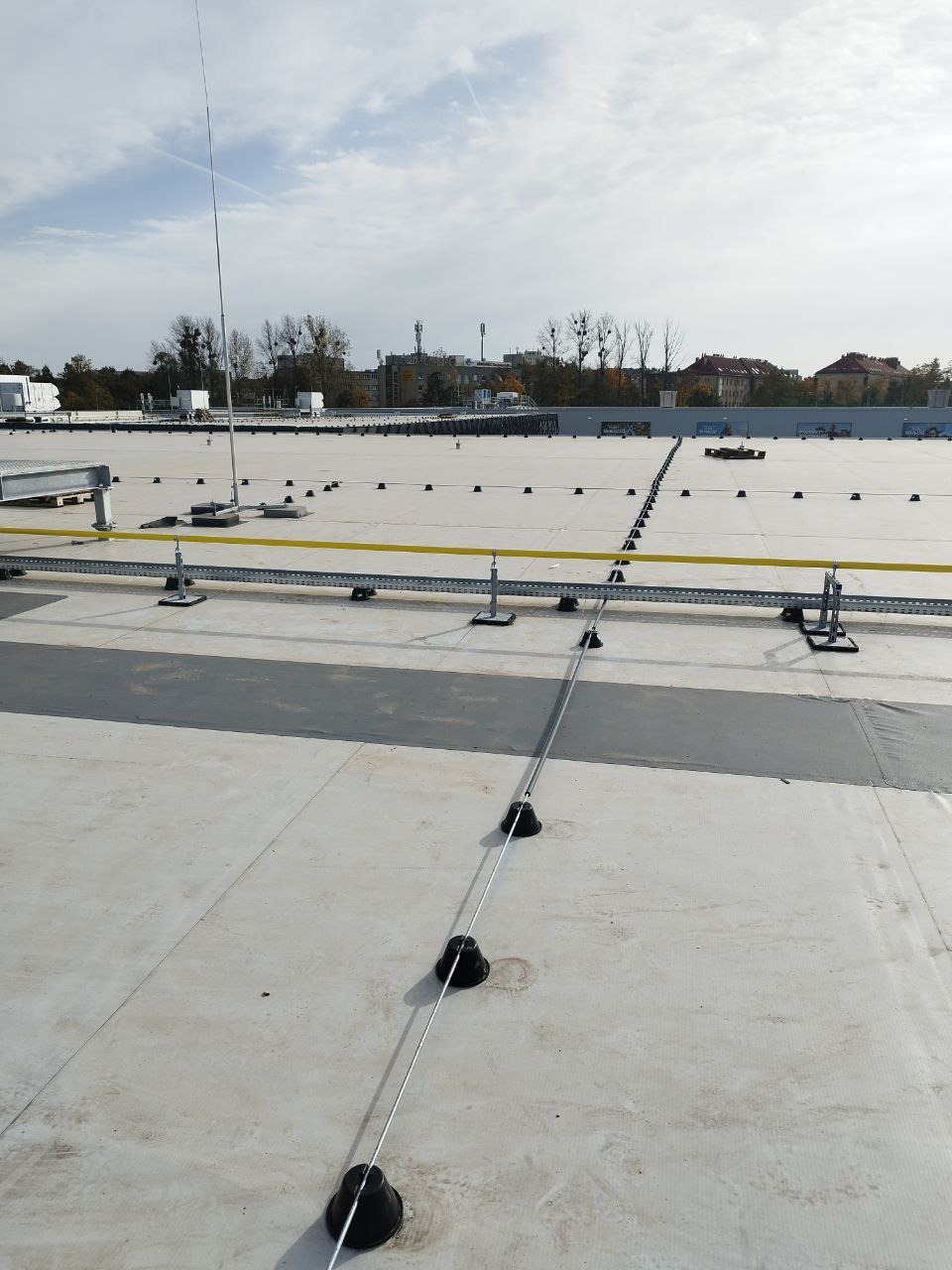Instalacja odgromowa na płaskim dachu budynku przemysłowego z widocznymi uchwytami i przewodami odprowadzającymi.