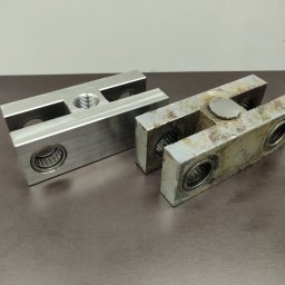 B4TECH JACEK WÓJCIK, JANUSZ KINE SPÓŁKA CYWILNA - Dwa metalowe elementy z łożyskami: jeden nowy, obrobiony CNC z gwintem, drugi stary, skorodowany. Porównanie stanu przed i po obróbce.