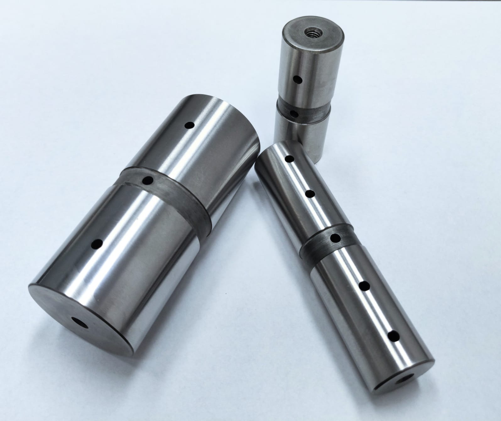 Metalowe, precyzyjnie obrobione cylindryczne elementy z otworami, widoczne ślady obróbki tokarskiej, na białym tle. Precyzja wykonania i dokładność detali.