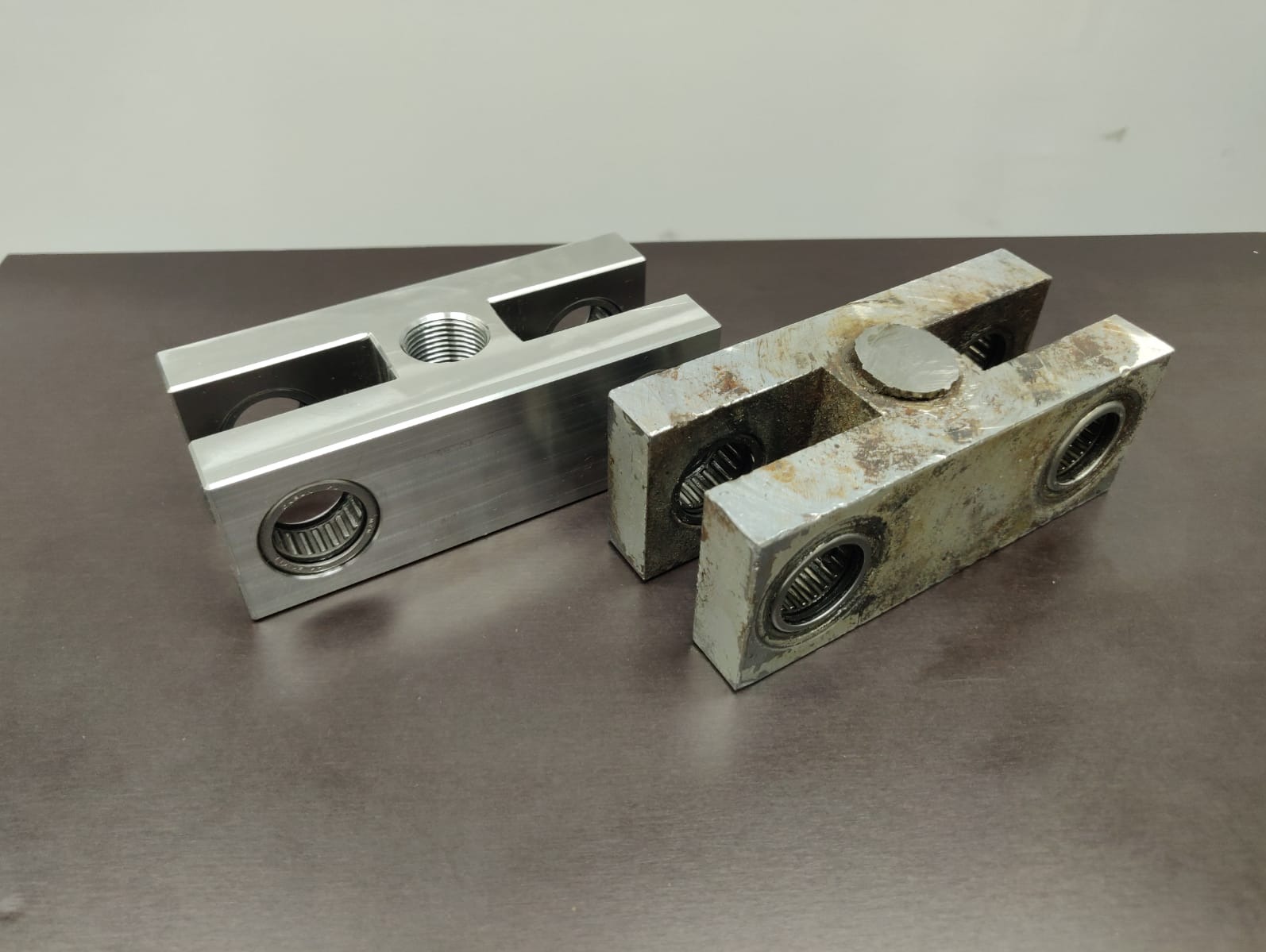 Dwa metalowe elementy z łożyskami: jeden nowy, obrobiony CNC z gwintem, drugi stary, skorodowany. Porównanie stanu przed i po obróbce.