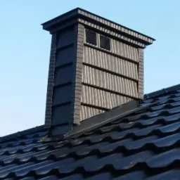 Nowoczesny komin wentylacyjny z szarej blachy trapezowej, dopasowany kolorystycznie do ciemnego dachu z blachodachówki, na tle błękitnego nieba.