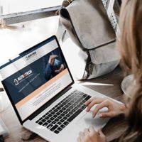 Kobieta pisząca na laptopie z otwartą stroną internetową firmy z branży instalacyjnej, widoczny plecak, jasne tło. Strona internetowa prezentuje firmę z logo i grafiką związaną z instalacjami.