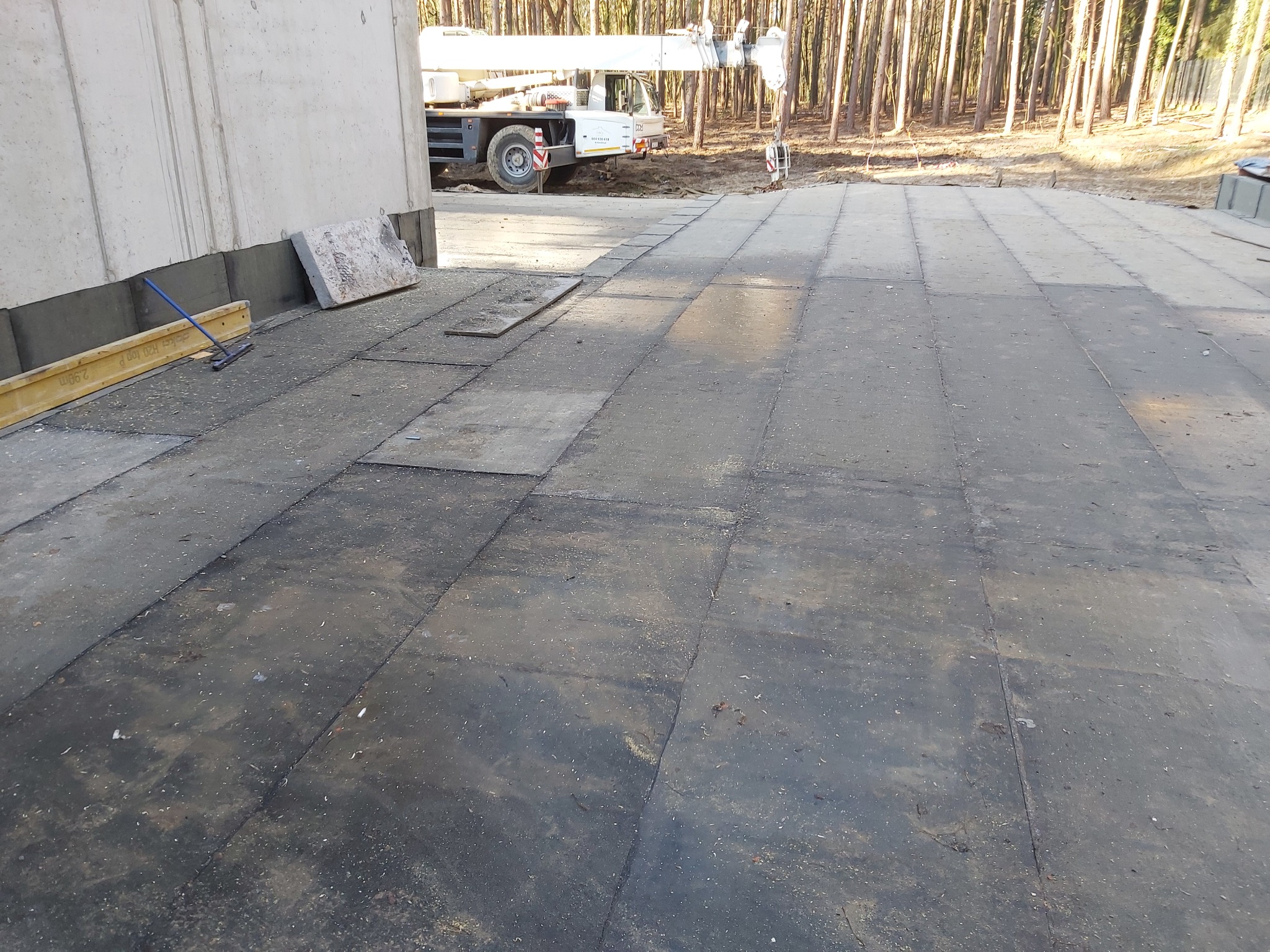 Przygotowanie podłoża dachowego z papy termozgrzewalnej, widoczny dźwig budowlany w tle i las.