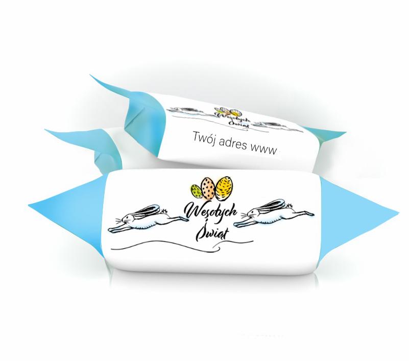 Dwa cukierki w błękitnych papierkach z nadrukiem wielkanocnym: zające, pisanki i napis 'Wesołych Świąt', jeden z nadrukowanym adresem strony internetowej.