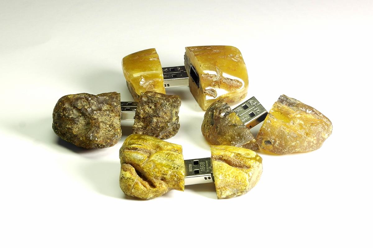 Ręcznie robione pendrive'y z bursztynu, każdy przecięty na pół, eksponujące metalowy element USB, ułożone na białym tle.