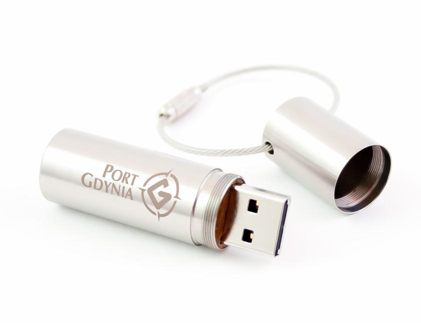 Metalowy pendrive z grawerowanym logo Port Gdynia, obok leży metalowa nakrętka z mocowaniem do smyczy