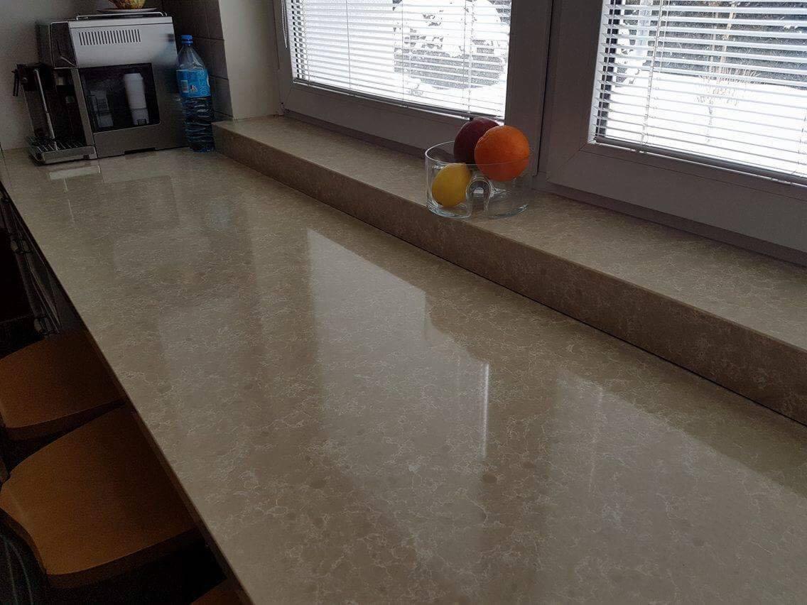 Jasny, błyszczący blat z konglomeratu w Zabłudowie, z owocami w szklanej misce pod oknem z żaluzjami.