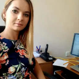 Portret kobiety w biurze, z monitorem, telefonem i notatkami na biurku, sugerujący pracę biurową lub konsultacje prawne.