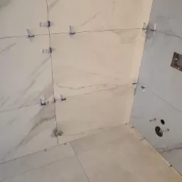 Układanie płytek imitujących marmur w łazience, widoczne krzyżyki dystansowe i otwory na instalacje.