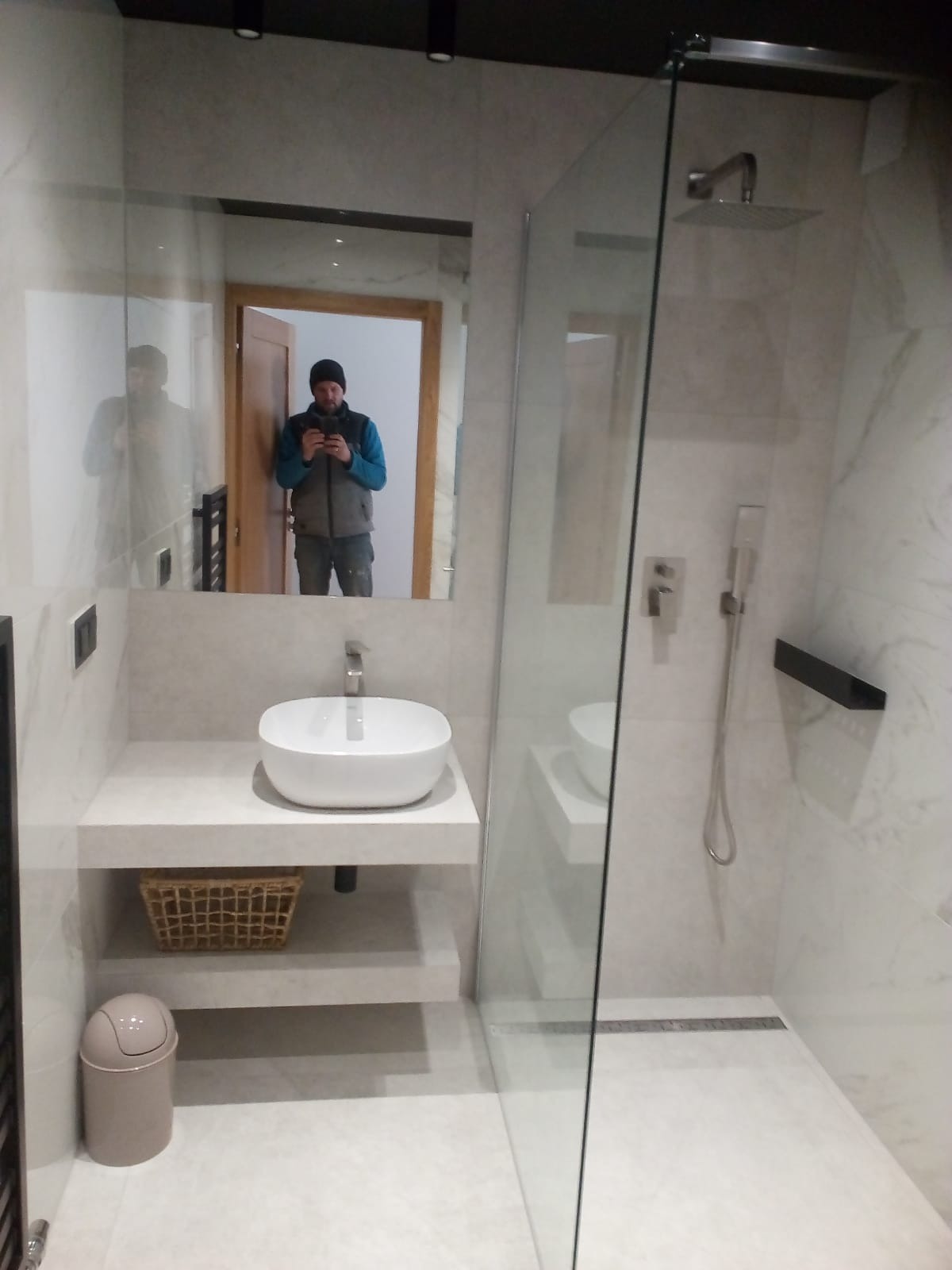 Nowoczesna łazienka z kabiną prysznicową typu walk-in, umywalką nablatową i lustrem, w którym odbija się osoba robiąca zdjęcie.