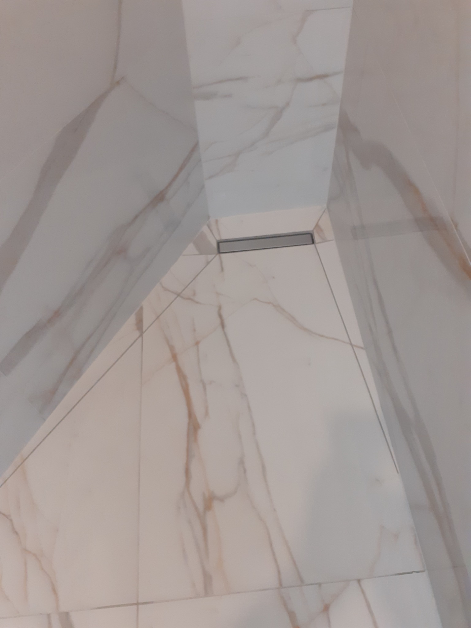 Wykończona łazienka z białymi płytkami imitującymi marmur i odpływem liniowym w podłodze.