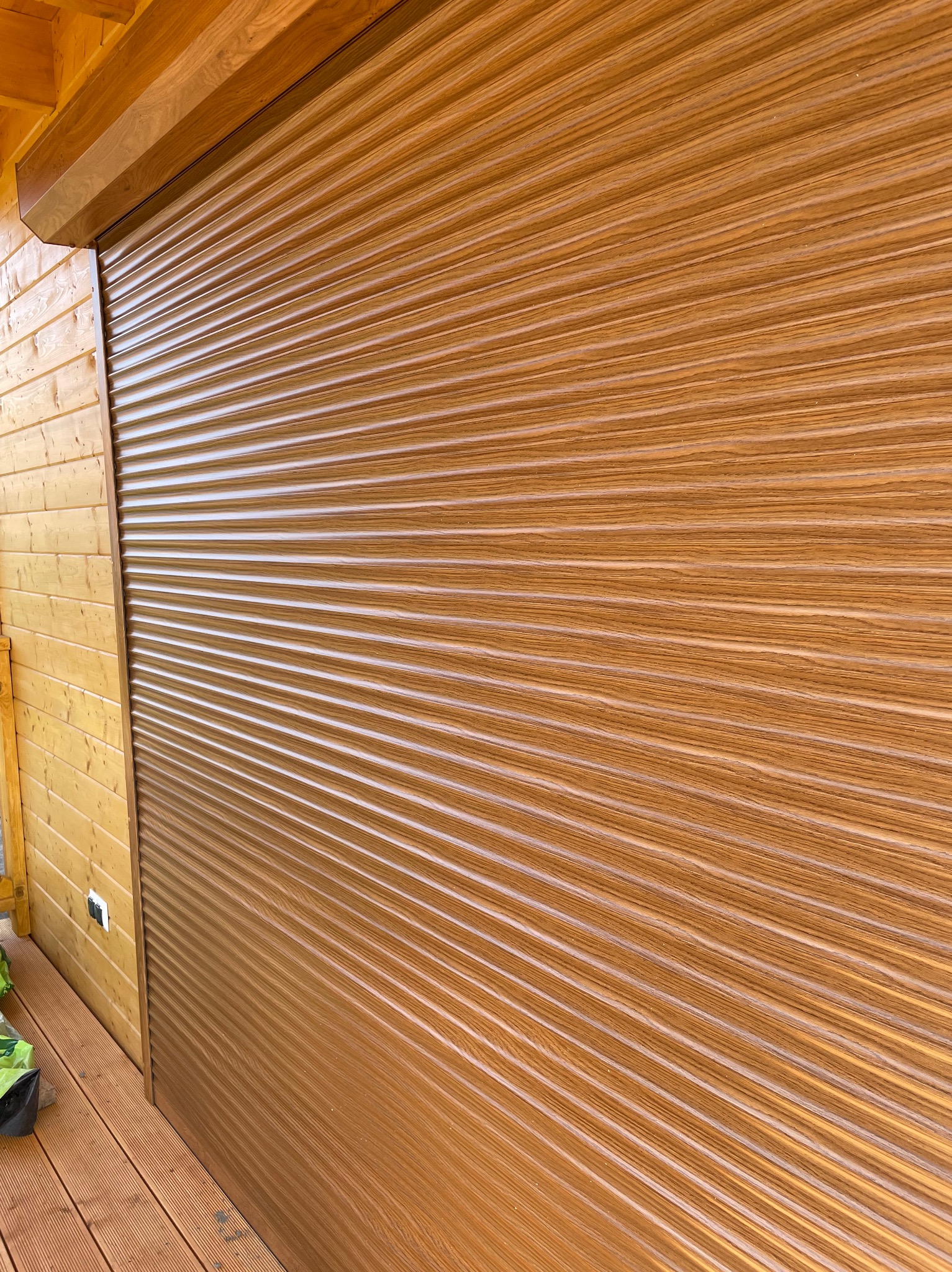 Zamknięta, brązowa roleta zewnętrzna na drewnianej elewacji budynku w Słupsku. Widoczna faktura drewna na rolecie i elewacji, kątowe ujęcie.