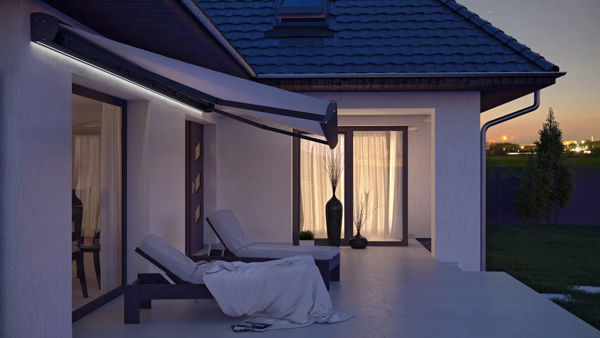 Elegancka, rozłożona markiza tarasowa z oświetleniem LED przy białym domu z dwoma leżakami na tarasie, widok wieczorny.