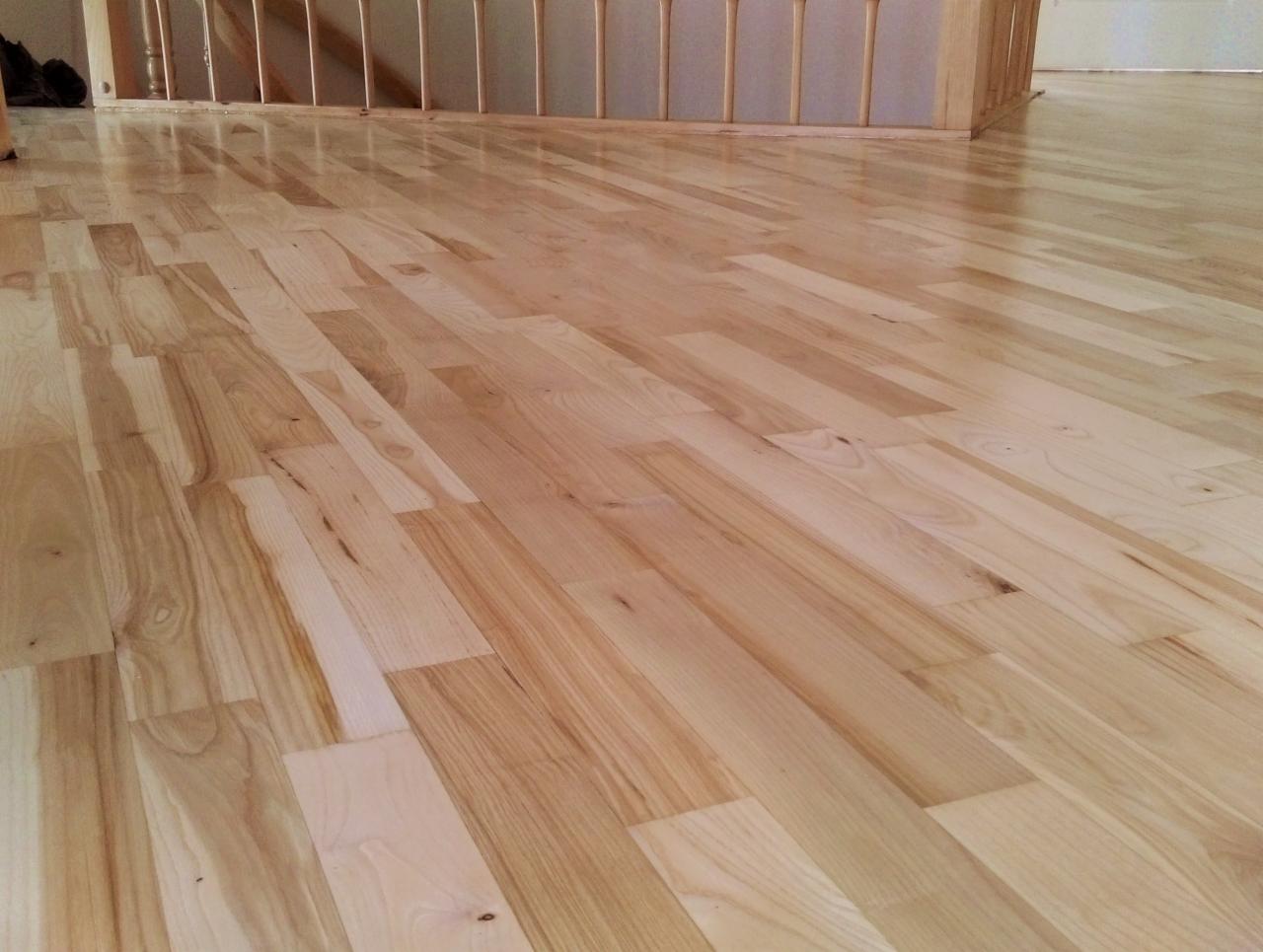 Świeżo ułożony, jasny parkiet z wyraźnym usłojeniem, widoczne fragmenty drewnianej balustrady schodów.