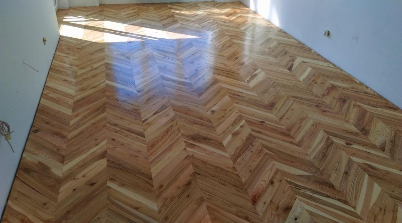Nowo ułożony parkiet w jodełkę z jasnego drewna, widoczne niedoskonałości na ścianie i świeże ślady po instalacji elektrycznej.