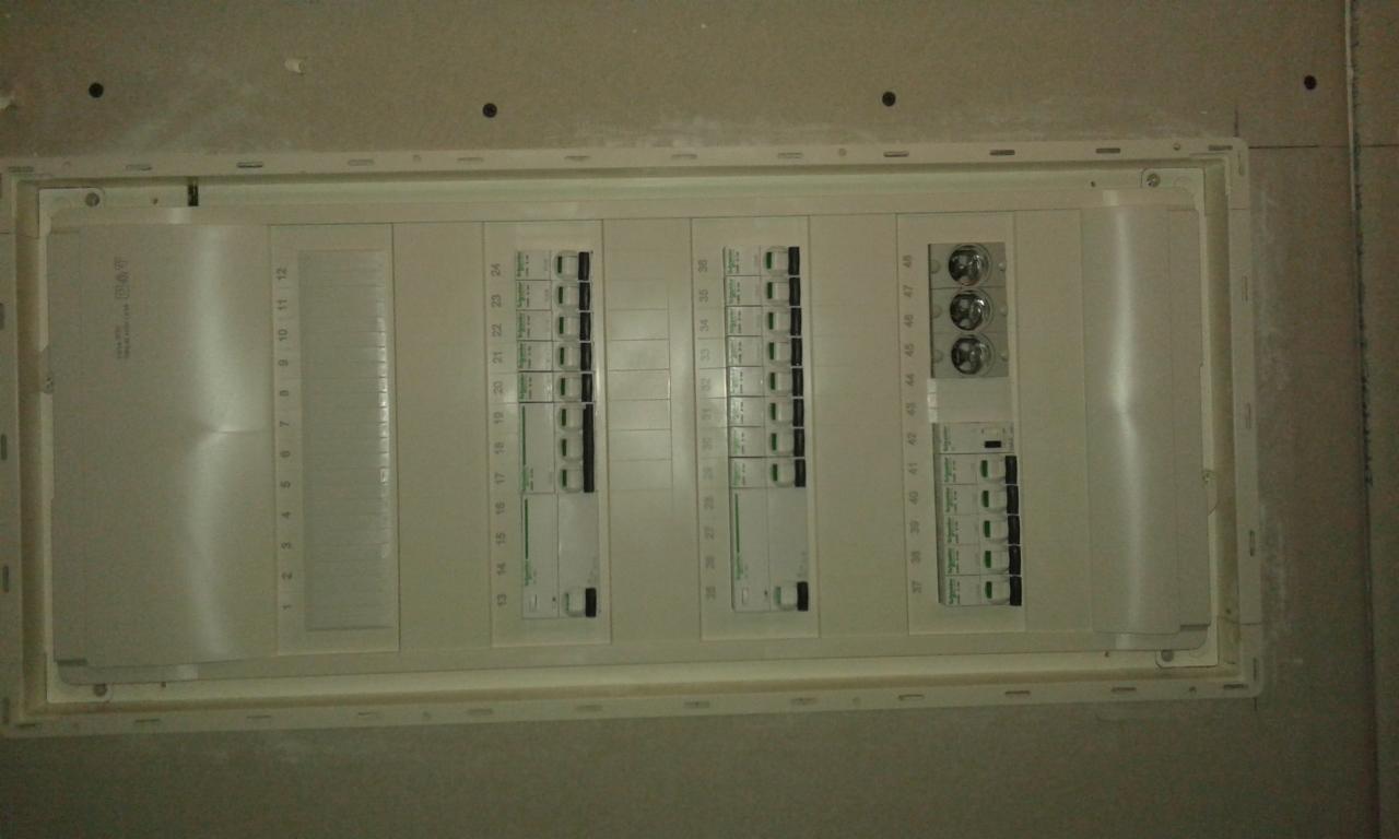 Zamknięta rozdzielnica elektryczna, widok na zabezpieczenia i wyłączniki, zamontowana w ścianie z płyt kartonowo-gipsowych przed finalnym wykończeniem.