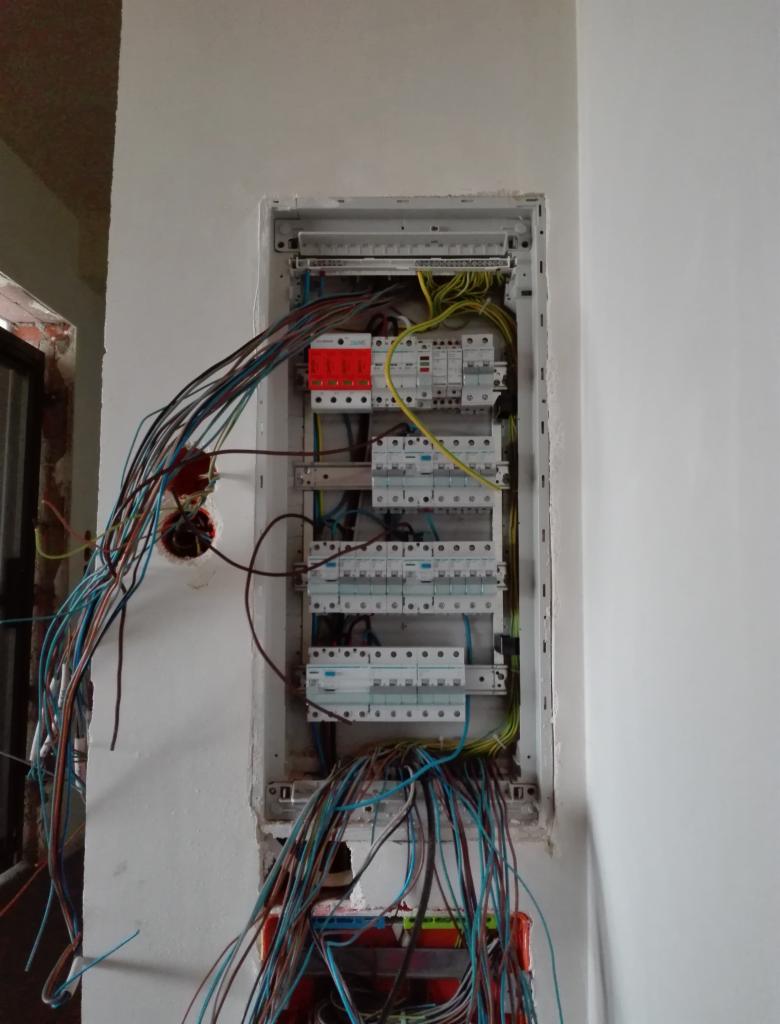 Rozdzielnica elektryczna w trakcie montażu w surowym stanie, widoczne liczne przewody i zabezpieczenia, ściany nieotynkowane.