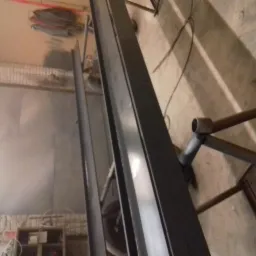 Metalowe profile po piaskowaniu, widoczne ślady obróbki i przygotowania do malowania proszkowego, surowe wnętrze warsztatu w tle.