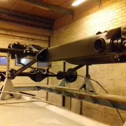 Podwozie samochodu, zawieszone na stojakach w warsztacie, po zabiegach antykorozyjnych z widocznym nowym czarnym lakierem.