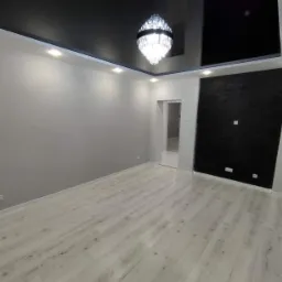 Pomalowane na szaro wnętrze z czarnym, błyszczącym sufitem podwieszanym, oświetleniem punktowym LED i ozdobną ścianą z czarnej cegły, z parkietem w odcieniach szarości i białym wykończeniem.