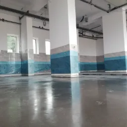 Świeżo wylana, błyszcząca, szara podłoga w hali przemysłowej z widocznymi śladami butów, zabezpieczone folią płytki na ścianach i kolumnach.