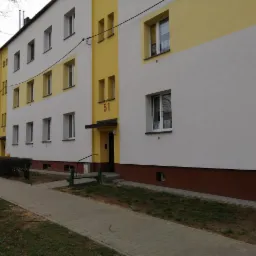 Wielorodzinny budynek z numerem 51, pomalowany na biało i żółto, z brązowym pasem u dołu, widziany z chodnika.