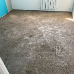 Wylewka samopoziomująca na podłodze w pomieszczeniu z niebieską ścianą, przygotowana pod dalsze prace wykończeniowe.