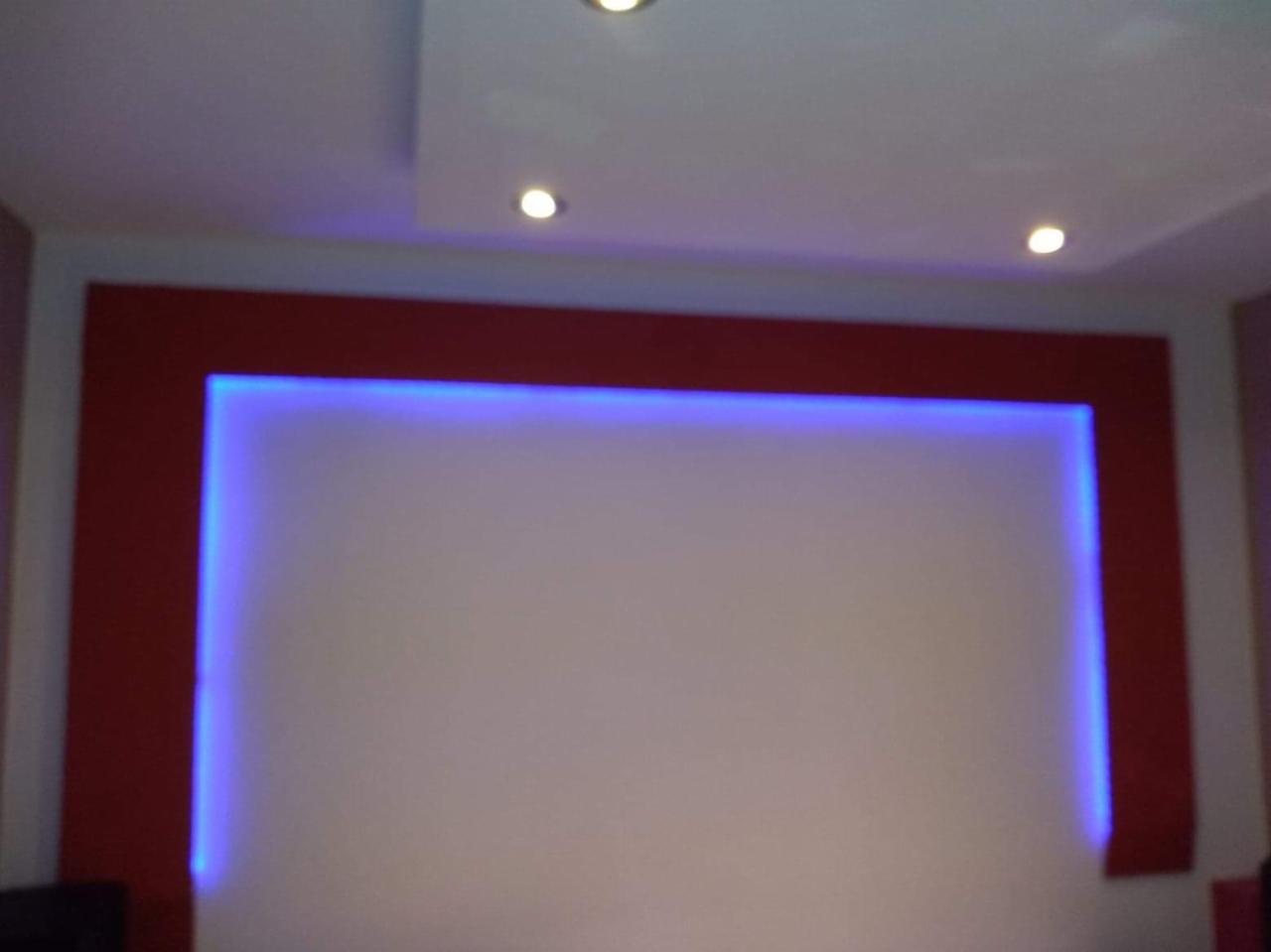 Ściana z podświetlanym na niebiesko wnęką, obramowana bordową ramą, oświetlona punktowymi lampami w suficie.
