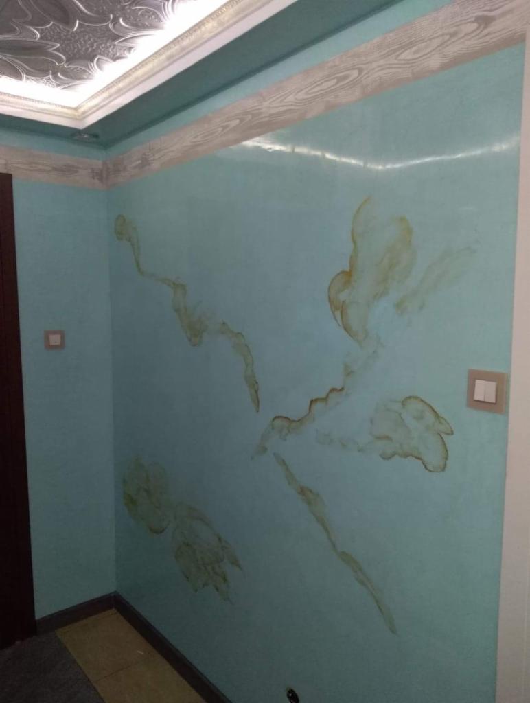 Turkusowa ściana z abstrakcyjnym, brązowym wzorem imitującym plamy i żyły kamienia, dekoracyjny sufit z ornamentami i listwą przypodłogową imitującą drewno.