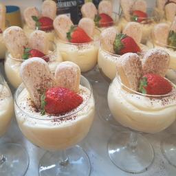 CFR plus Pychotki - Deser w szklance na nóżce: kremowy pudding z truskawką i biszkoptami oprószonymi kakao, ustawiony w rzędach z innymi porcjami.