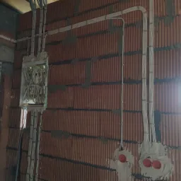Wewnętrzna instalacja elektryczna w trakcie montażu w budynku z czerwonej cegły, widoczne kable prowadzone po ścianach i puszka instalacyjna z przewodami.
