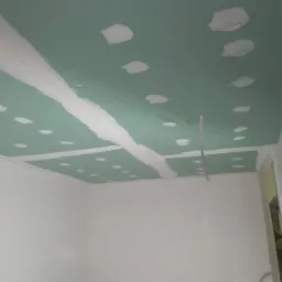 Zielona płyta gipsowo-kartonowa na suficie z widocznymi białymi paskami gładzi na łączeniach i w miejscach wkrętów, na ścianach widoczna biała farba.