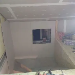 Poddasze w trakcie adaptacji: ocieplenie wełną mineralną widoczne na ścianie, płyty gipsowo-kartonowe zamontowane na suficie i ścianach, otwór okienny w ścianie szczytowej, narzędzia budowlane...