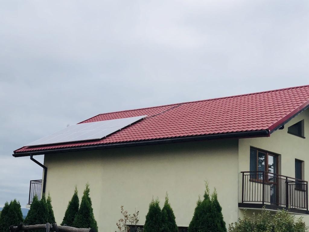 Panele słoneczne na czerwonym dachu domu jednorodzinnego, widok z dołu, pochmurne niebo.