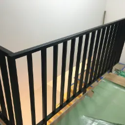 Nowoczesna, czarna balustrada schodowa z pionowymi szczeblami, widoczna podczas montażu, z zabezpieczeniami podłogi i schodów.