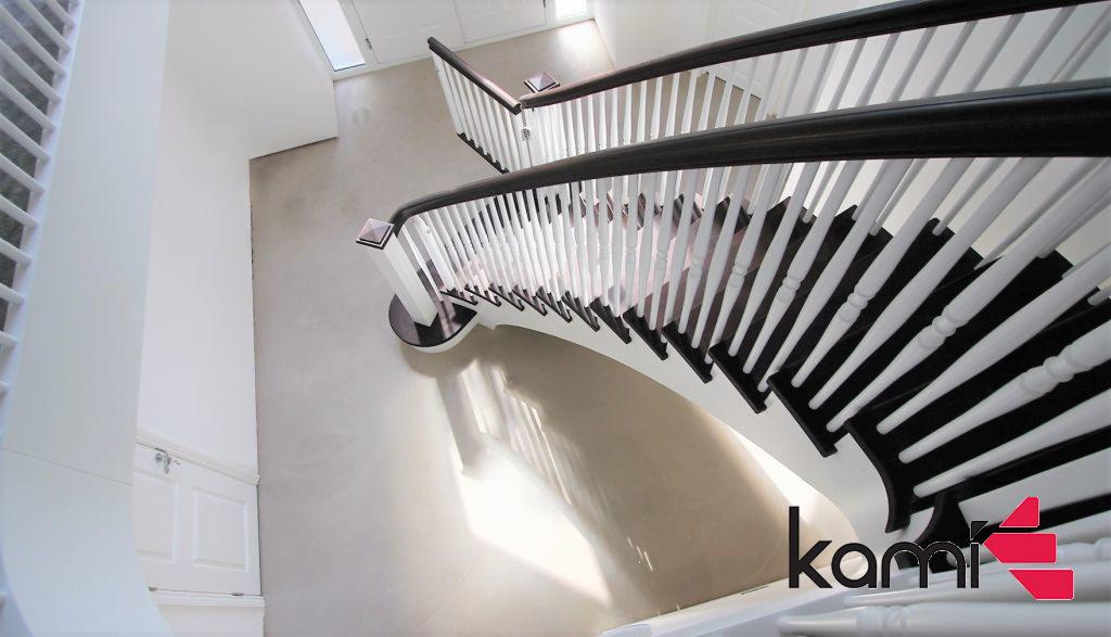 Nowoczesne schody z białymi balustradami i ciemnobrązowymi poręczami, widok z góry, z widocznym logo firmy w prawym dolnym rogu.