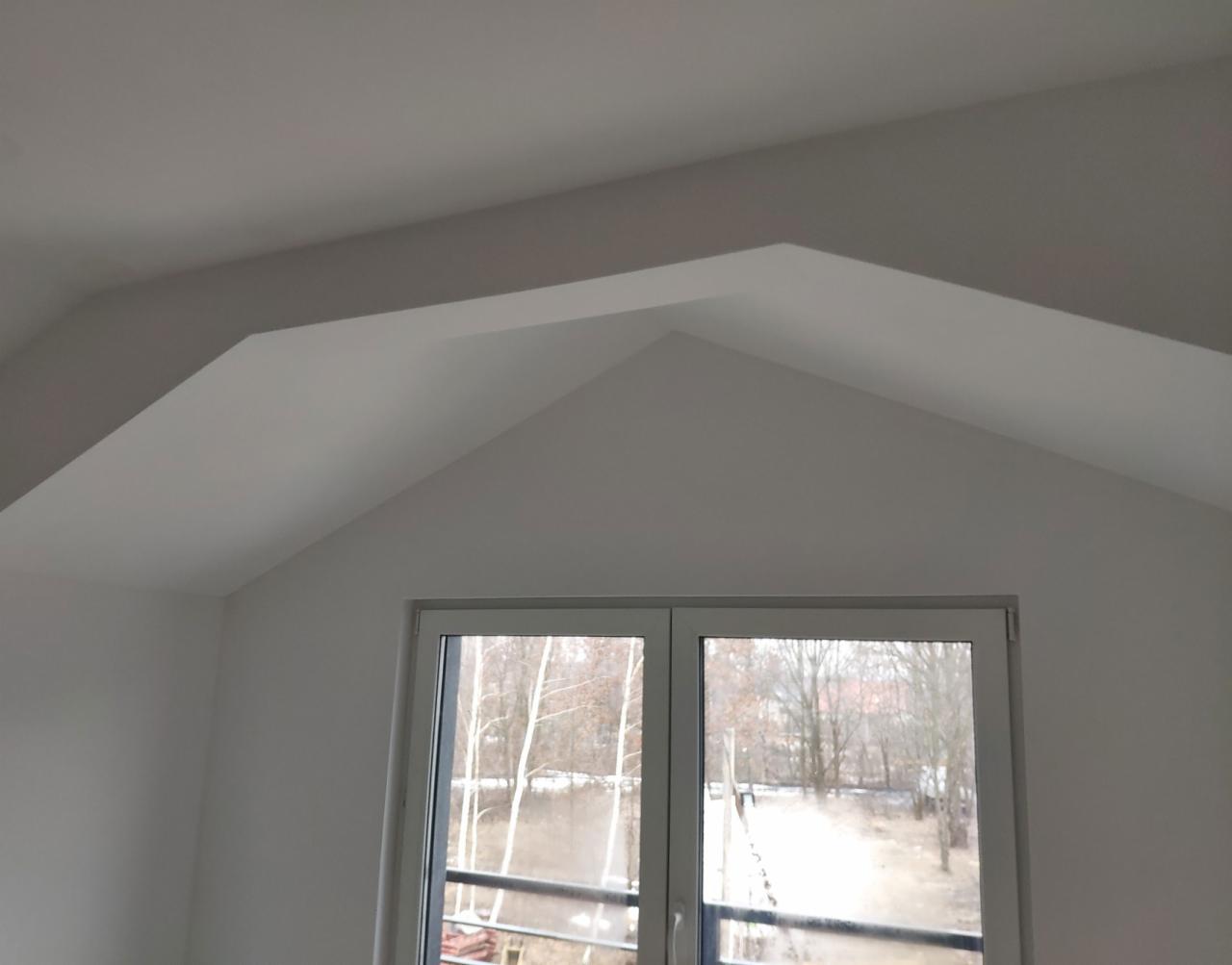 Świeżo pomalowane na biało poddasze z oknem PCV, widok na drzewa bez liści za oknem.