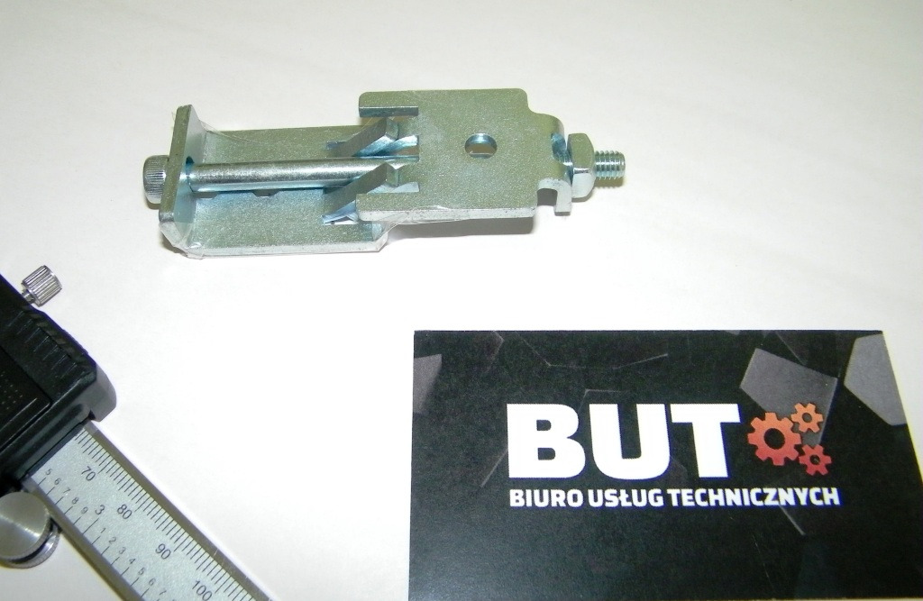 Metalowy uchwyt z gwintem, mierzony suwmiarką, obok wizytówka 'BUT Biuro Usług Technicznych'.