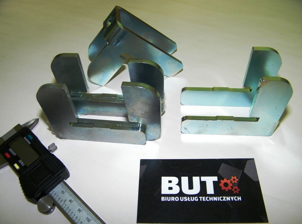 Metalowe elementy spawane lub obrabiane, pomiar suwmiarką elektroniczną, wizytówka Biura Usług Technicznych w tle.