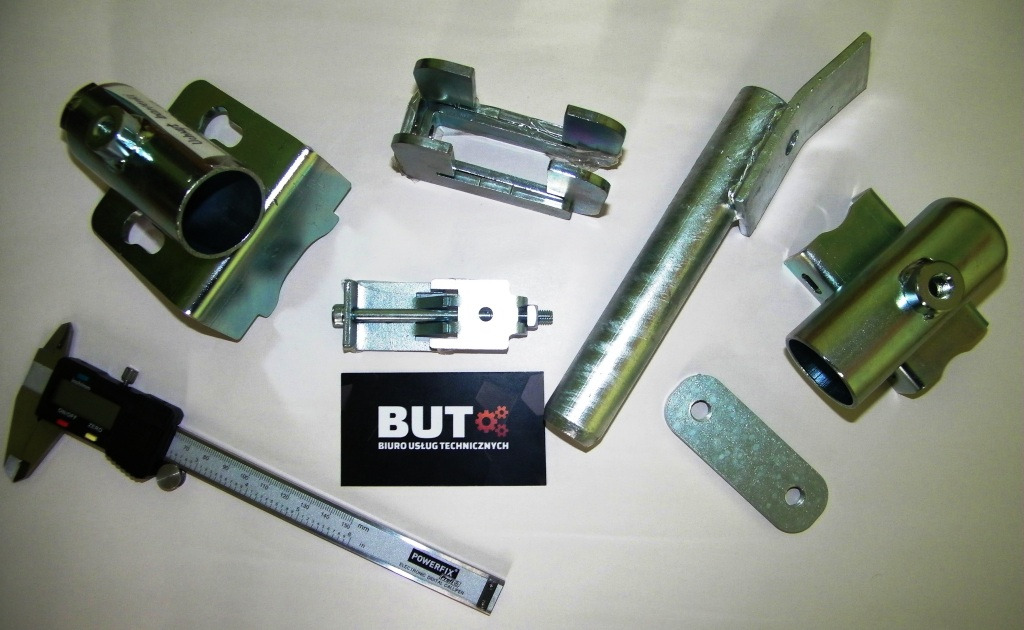 Metalowe elementy po obróbce, leżące obok cyfrowej suwmiarki i wizytówki firmy Biuro Usług Technicznych, widoczne ślady po procesie galwanizacji.