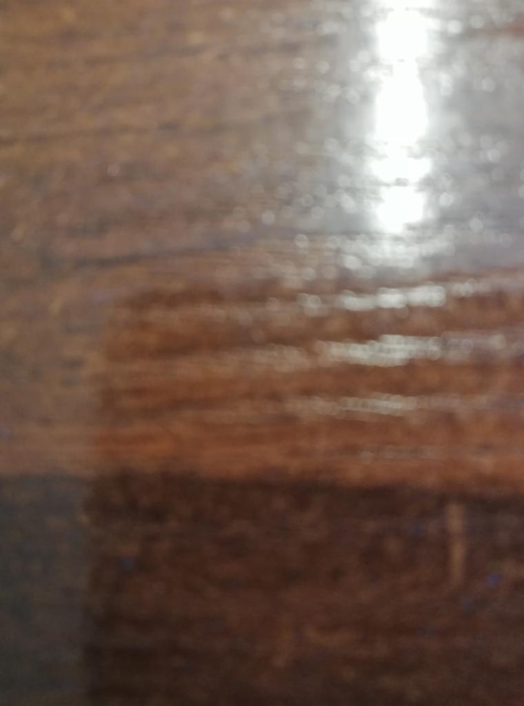 Rozmazane ujęcie lakierowanej, drewnianej powierzchni z widocznym odbiciem światła.