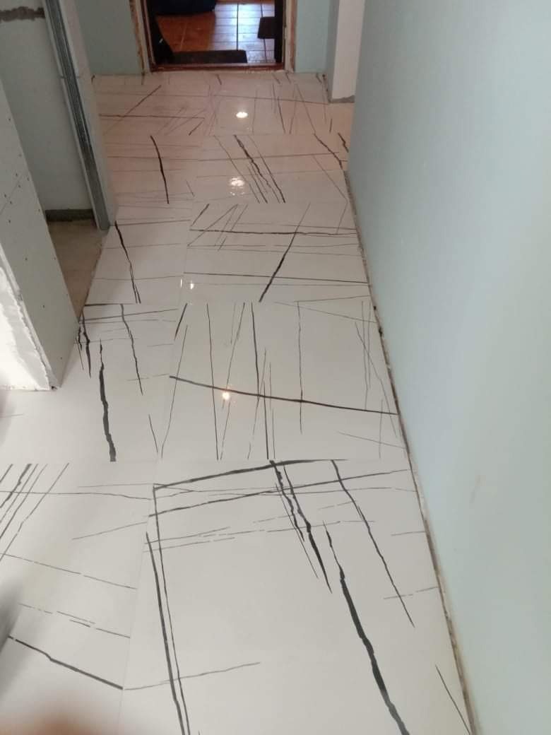 Nowa, błyszcząca podłoga z białych płytek ceramicznych z szarymi, nieregularnymi wzorami imitującymi marmur, ułożona w korytarzu, widok z góry.