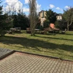 Ustawione na trawniku drewniane stoły i ławki, gotowe na przyjęcie gości w ośrodku wypoczynkowym.