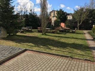 Ustawione na trawniku drewniane stoły i ławki, gotowe na przyjęcie gości w ośrodku wypoczynkowym.