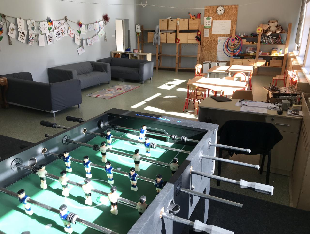 Sala zabaw z piłkarzykami, sofami, stolikami i dekoracjami dziecięcymi na ścianach, oświetlona naturalnym światłem.