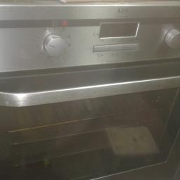 serwis AGD - Metalowy piekarnik marki AEG z widocznym panelem sterowania i uchwytem, obok leży wiertarka i kabel zasilający.